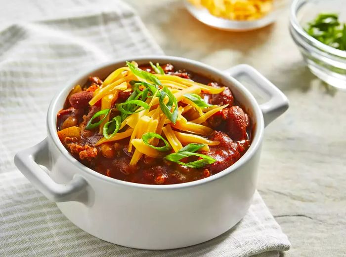 high-angle shot of a small bowl of chili garnished with green onions and shredded cheddar cheese