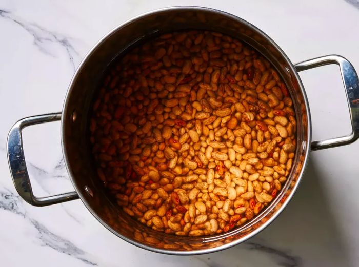 A large pot filled with dried pinto beans submerged in water