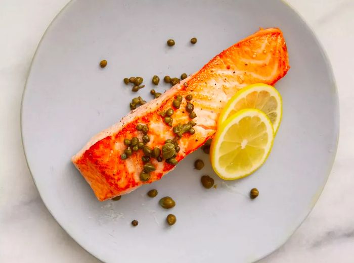 The salmon is ready, garnished with capers and a few lemon slices on top.