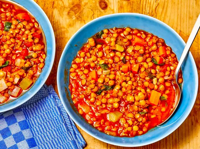 Aerial shot of two blue bowls filled with lentil soup, each with a spoon on the side