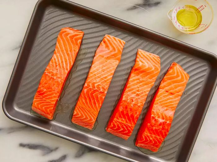 Salmon fillets placed skin-side down, coated with olive oil, ready to cook.