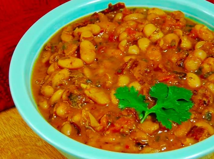 A bowl of pinto beans topped with tomatoes and bacon, elegantly garnished with a fresh sprig of cilantro.