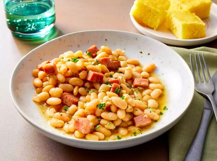 A bowl of ham and beans garnished with chopped parsley, served alongside cornbread