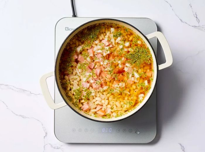 A large pot containing great northern beans, ham, onion, sugar, parsley, and cayenne pepper