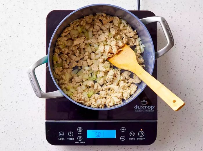 A large pot with browned ground turkey and chopped onion, being stirred with a wooden spoon.