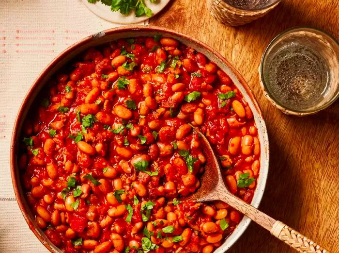 A serving bowl filled with pinto beans seasoned with Mexican spices, topped with freshly chopped cilantro, accompanied by a large wooden serving spoon