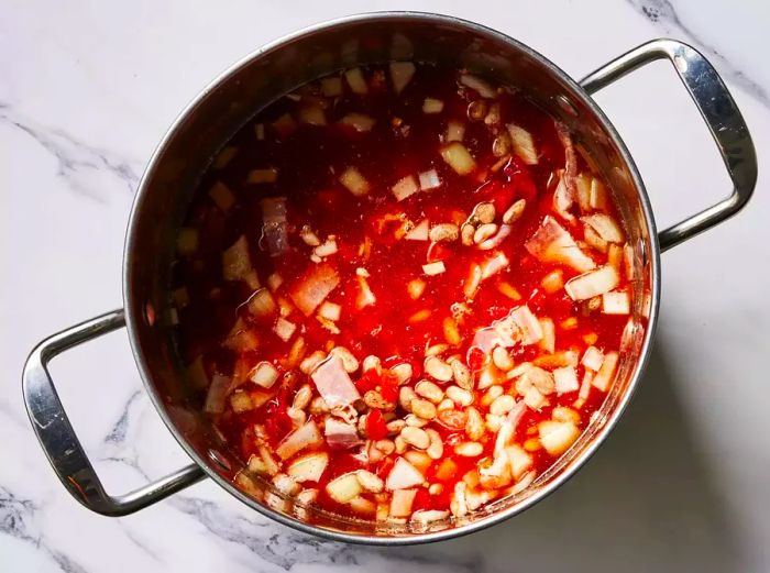 A pot of pinto beans in water, mixed with tomatoes, bacon, onion, chili powder, cumin, and garlic powder.