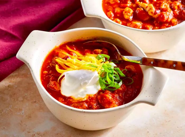 A bowl of turkey chili topped with sour cream, shredded cheese, and fresh green onion slices.