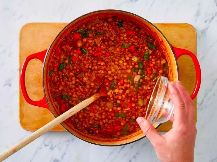 Overhead shot of hand pouring vinegar into the simmering lentil soup