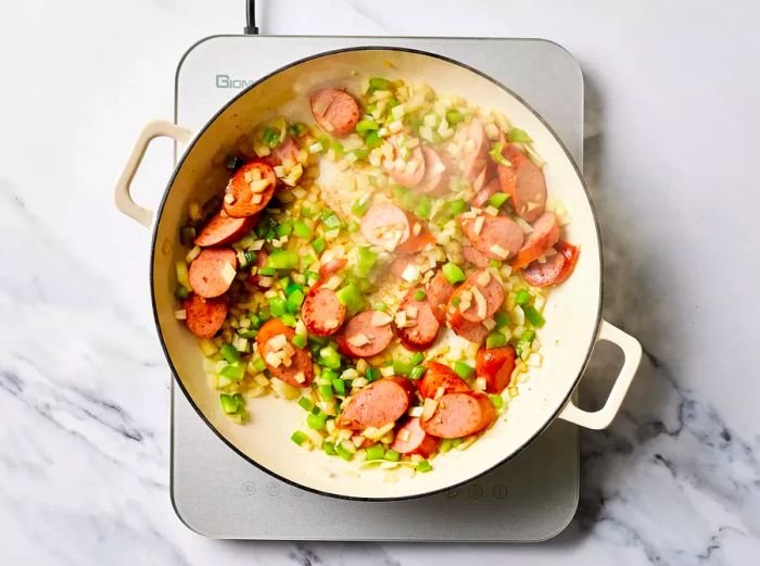 Onions, peppers, and sausage cooking together in a skillet.