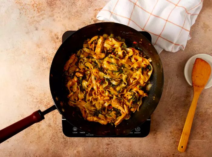 Noodles, vegetables, sliced chicken, and drunken noodle sauce mixed together in a wok.