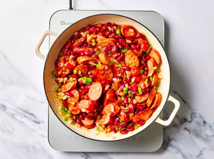 Red beans, vegetables, and sausages gently simmering in a pan on the stove.