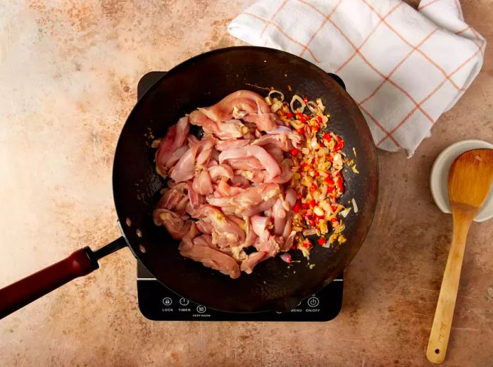 Sliced chicken breasts and vegetables in a wok.