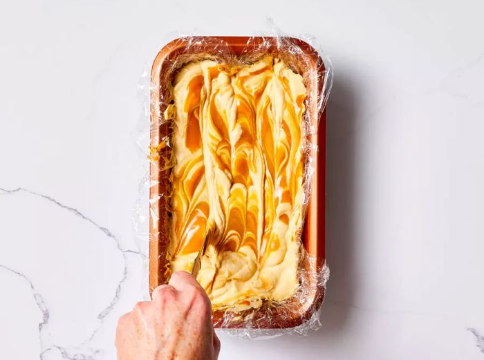 Decorating the top of the Dulce De Leche Ice Cream in a loaf pan, covered with plastic wrap