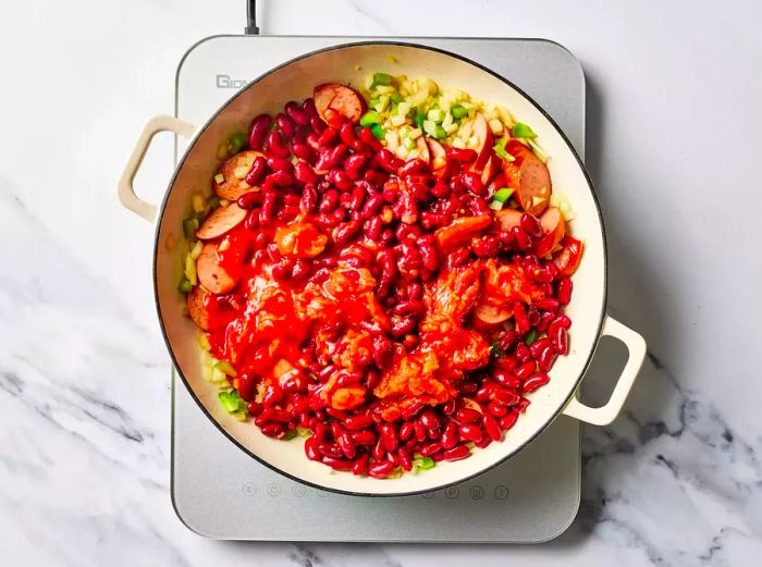 Adding red beans and tomatoes to the skillet with the sausage.