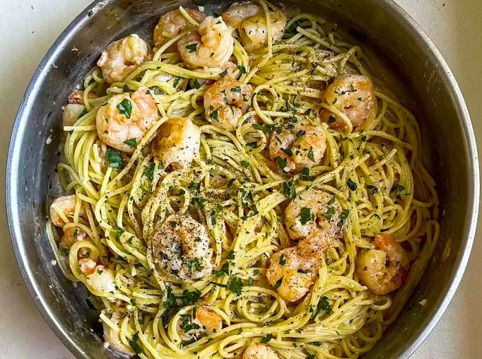 A top-down view of a skillet filled with creamy shrimp scampi, garnished with freshly cracked black pepper and chopped parsley