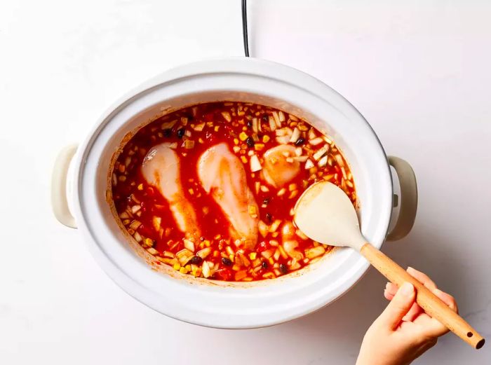 A slow cooker filled with chicken breasts resting on top of a bean and tomato mixture.