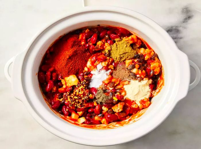 A slow cooker filled with turkey chili, garnished with spices and seasonings