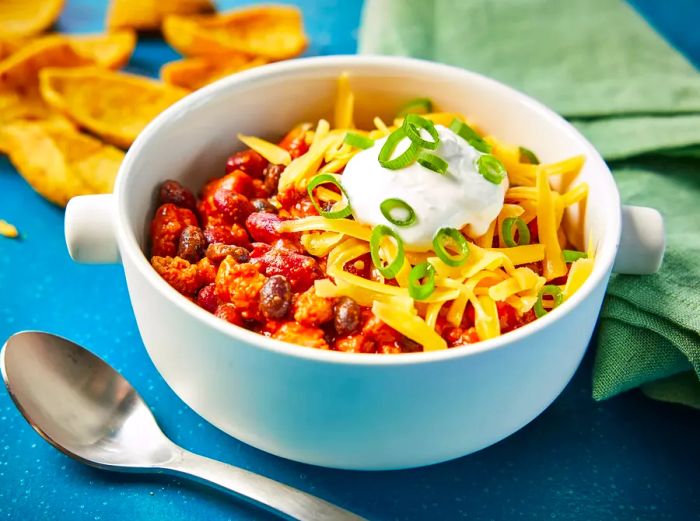 A bowl of Laura's quick turkey chili, topped with shredded cheese, sliced green onions, and a dollop of sour cream