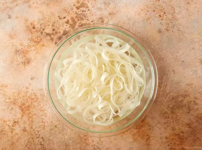 Rice noodles soaking in a glass bowl filled with water.