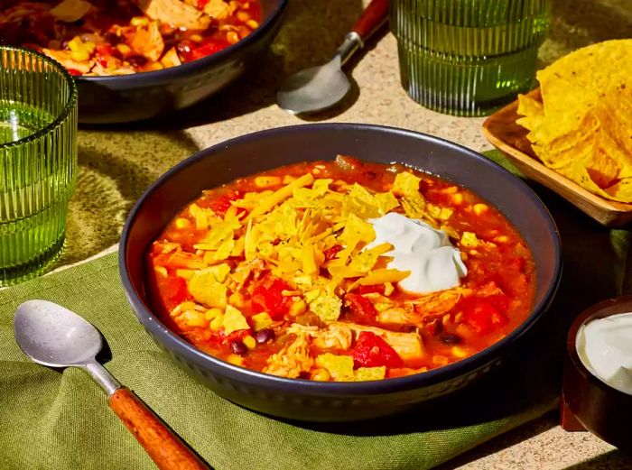 A bowl of slow cooker chicken taco soup, topped with sour cream and crushed tortilla chips.