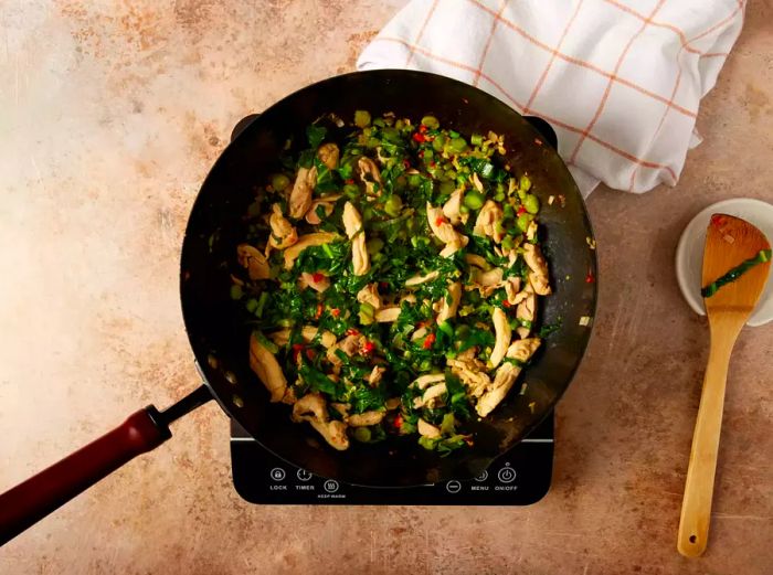 Sliced chicken and vegetables cooking together in a wok.