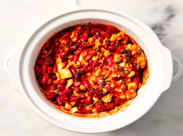 A slow cooker filled with turkey, tomato soup, kidney beans, black beans, and onion