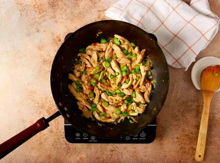 Sliced chicken and vegetables cooking in a wok.