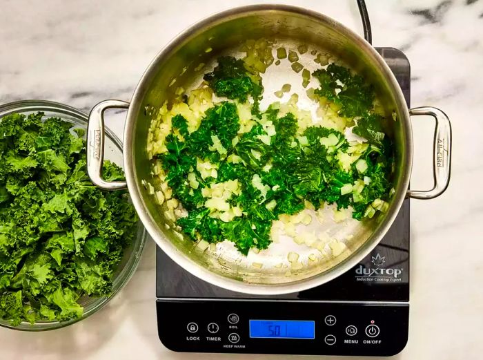 A large pot filled with chopped garlic, onion, and wilted kale