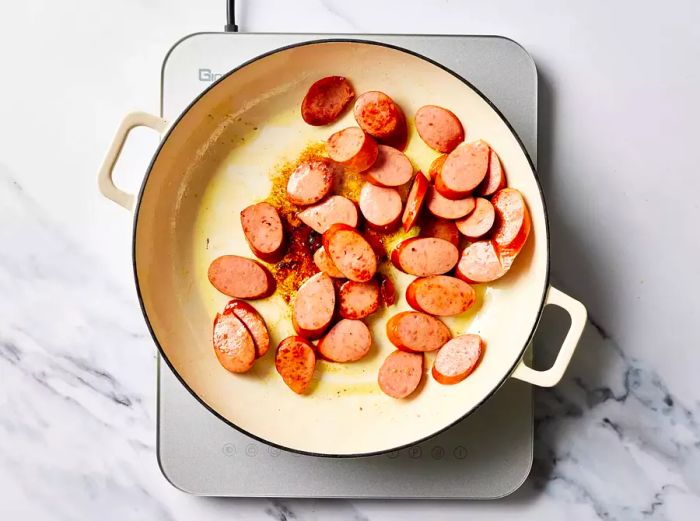 Sliced sausages sizzling in a pan on the stove.