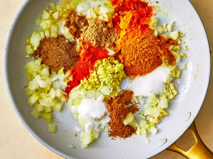 Onion, garlic, ginger, curry powder, cumin, turmeric, coriander, cayenne, and water cooking together in a skillet.