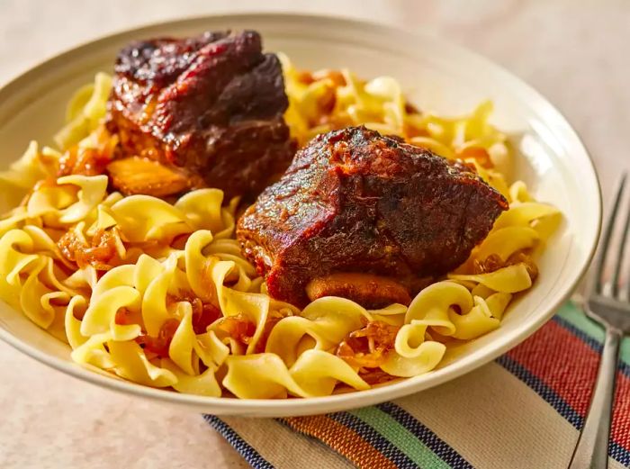 Two short ribs served in a bowl with egg noodles.