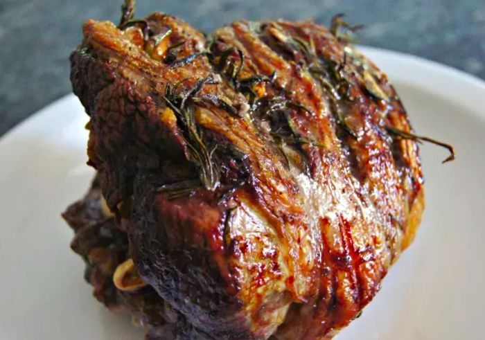 A beautifully roasted lamb leg, garnished with rosemary, served on a white platter.