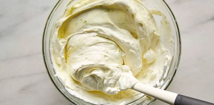 A rubber spatula gently folding soft whipped cream in a bowl.