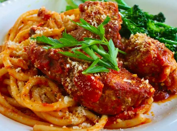 A close-up shot of Italian Country-Style Ribs served over pasta, topped with fresh herbs, accompanied by a side of broccoli rabe in a white bowl.