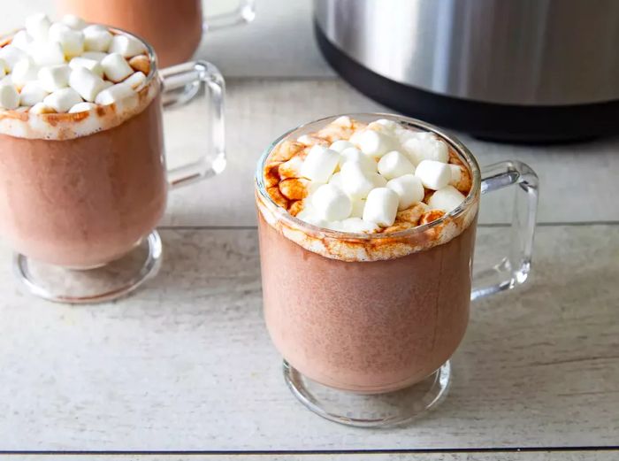 A top-down view of two clear mugs filled with creamy hot cocoa, each topped with melting mini marshmallows.