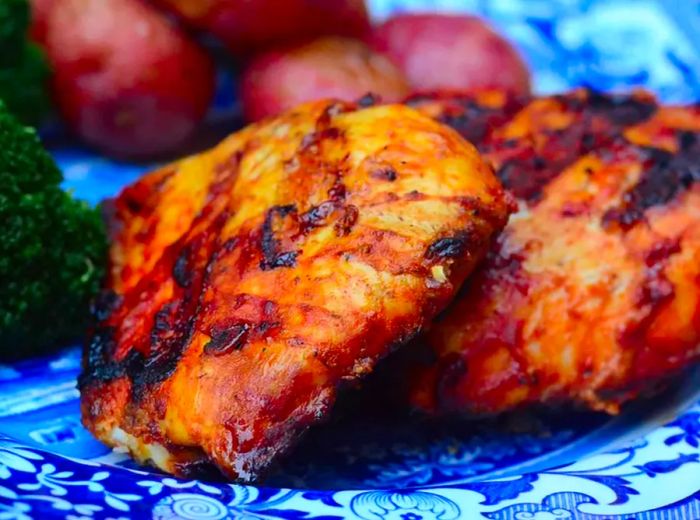 close-up of tender, grilled chicken breasts on a vibrant blue plate with red potatoes and fresh broccoli in the background