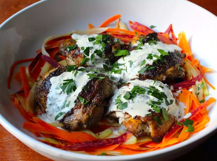 four perfectly grilled chicken thighs drizzled with Chef John's signature Alabama-Style White Barbecue Sauce, topped with fresh parsley and served in a bowl on a bed of crisp shaved carrot salad