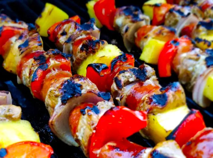 close-up of skewers featuring chicken, red bell peppers, pineapple chunks, and chorizo sausage grilling to perfection