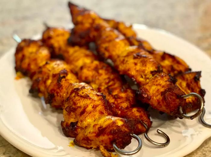 close-up of golden-brown Turkish Chicken Kebabs on metal skewers, neatly stacked on a white plate