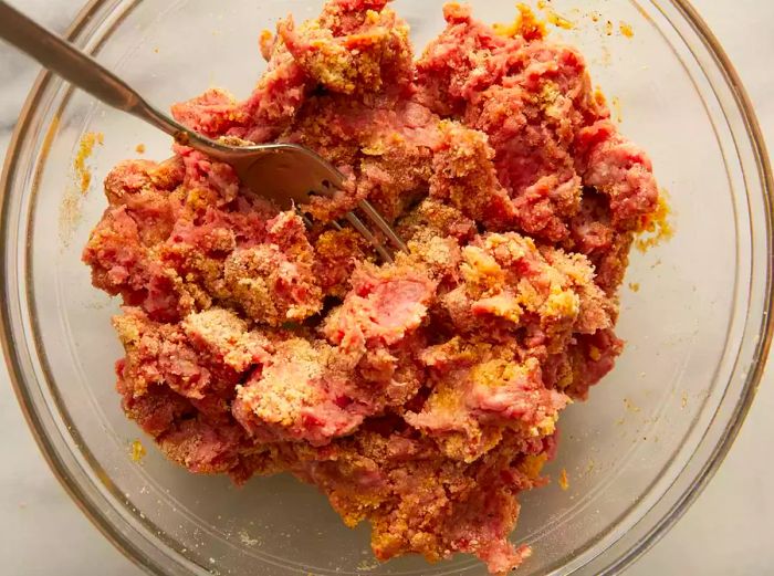 Top-down view of ground meat being combined with other burger ingredients