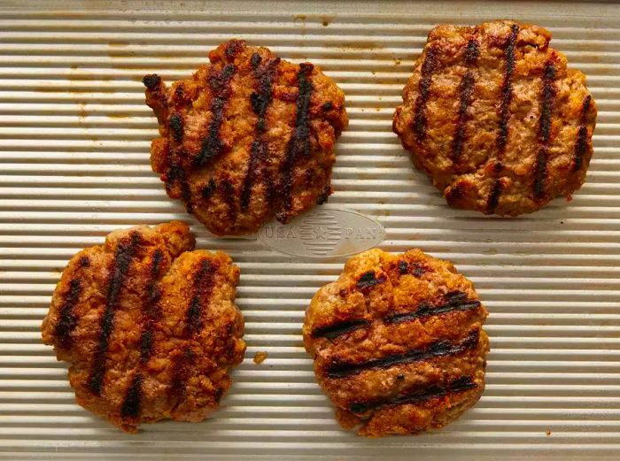 Top-down view of grilled burgers resting on a baking sheet