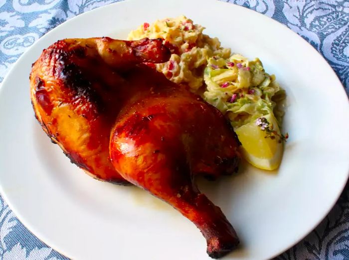 a perfectly grilled, golden-brown chicken half (Chef John's Buttermilk Barbecue Chicken) on a white plate, accompanied by potato salad and coleslaw