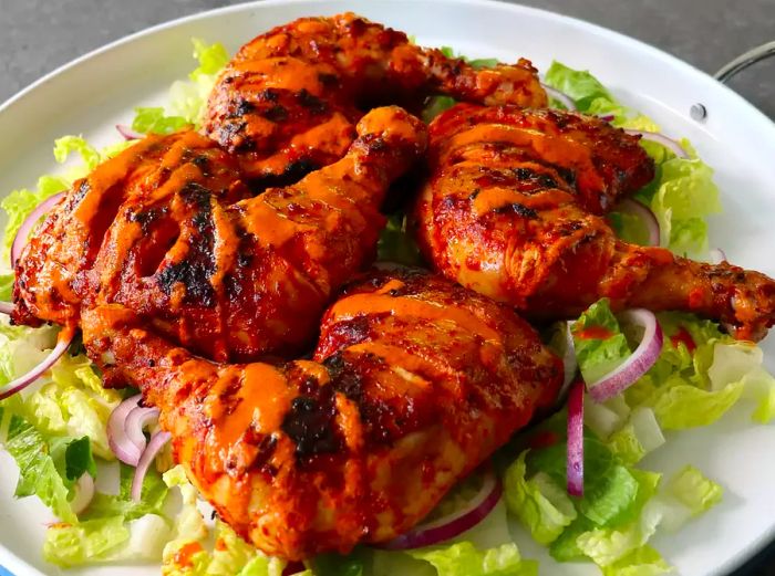 four grilled chicken drumsticks drizzled with Chef John's fiery Peri Peri sauce, resting on a bed of fresh greens