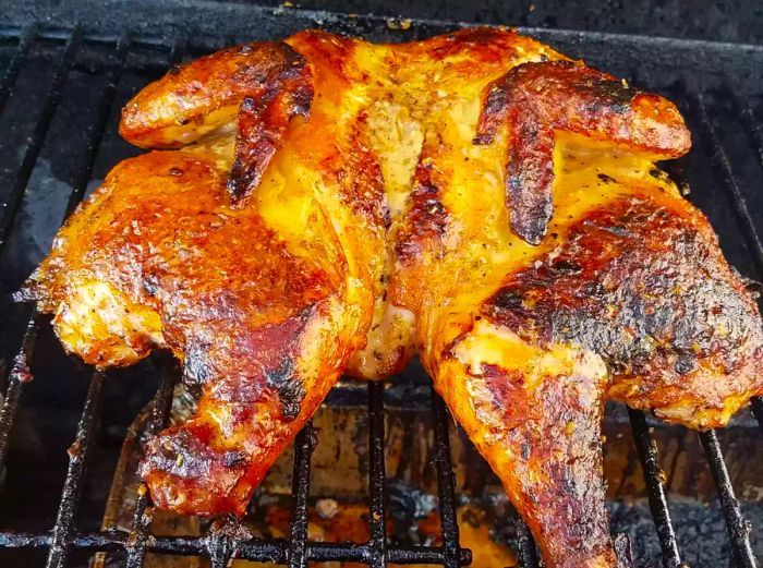 close-up of a whole butterflied chicken grilled to perfection with Chef John's Calabrian Chicken marinade on the grill grate