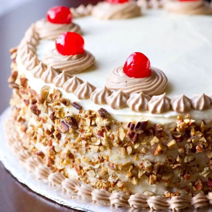 A beautiful Italian Cream Cake adorned with chopped nuts and cherries for an extra touch of elegance.