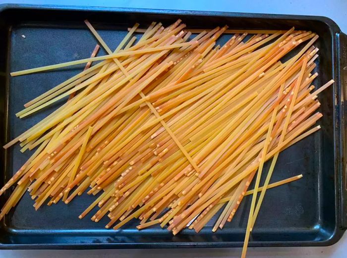 Toasted, dry fettuccine spread out on a baking sheet