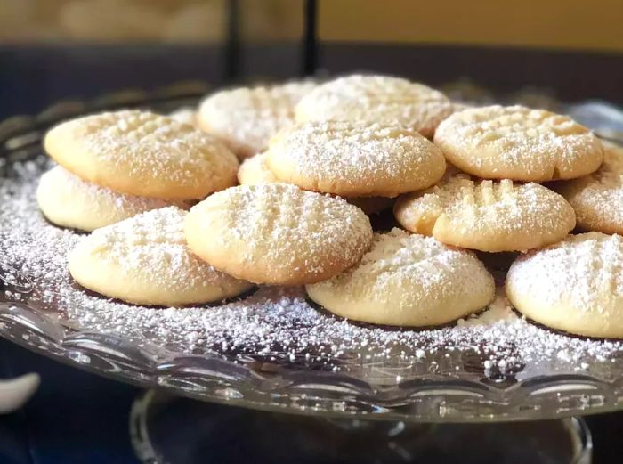 A close-up view of a plate of Melting Moments cookies, dusted with powdered sugar and beautifully arranged.