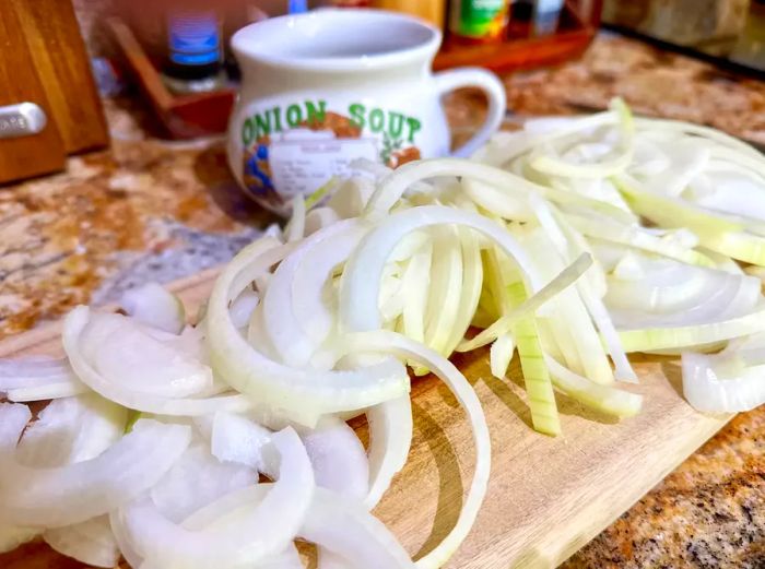 Sliced onions laid out on a cutting board next to a vintage onion soup bowl