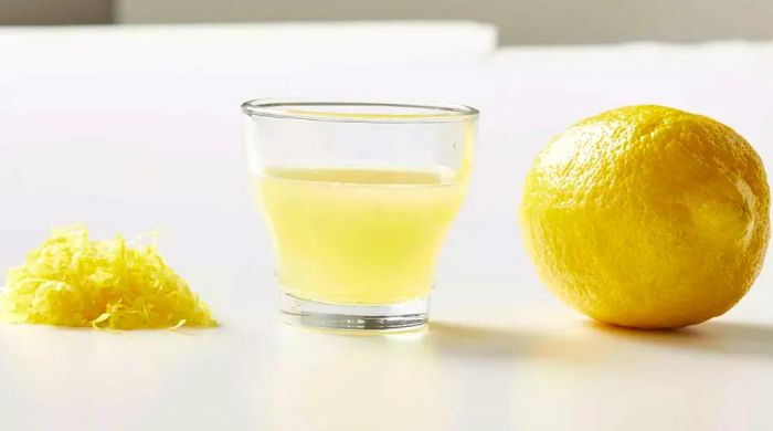 A heap of lemon zest next to a cup of lemon juice and a whole lemon